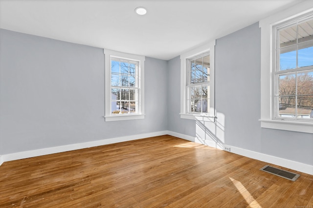 unfurnished room with a wealth of natural light, visible vents, baseboards, and wood finished floors