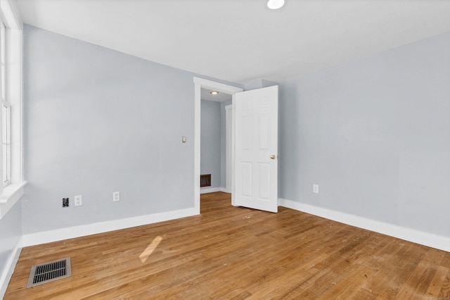 empty room with wood finished floors, visible vents, and baseboards