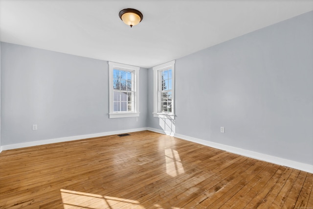 unfurnished room with visible vents, baseboards, and hardwood / wood-style flooring