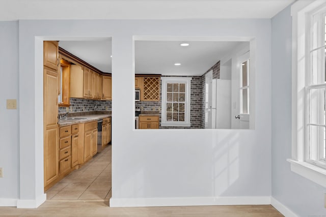 kitchen featuring light countertops, backsplash, freestanding refrigerator, dishwasher, and baseboards