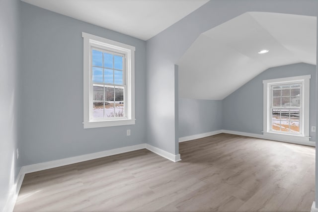 additional living space featuring light wood finished floors, baseboards, and vaulted ceiling