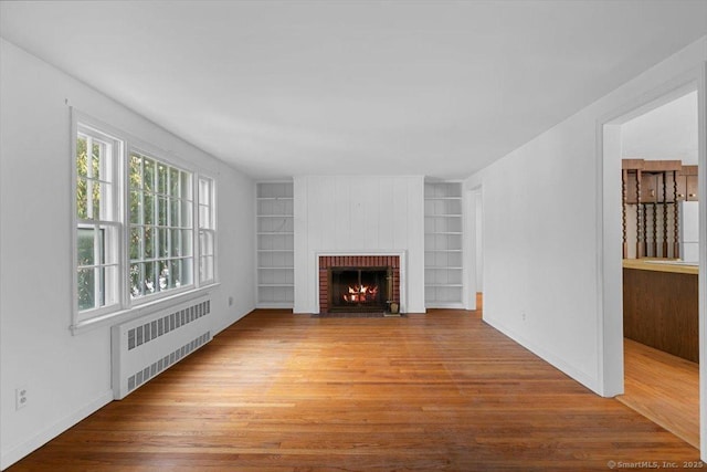 unfurnished living room featuring radiator heating unit, a brick fireplace, wood finished floors, and built in features