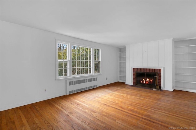 unfurnished living room featuring built in features, a brick fireplace, radiator, and wood finished floors