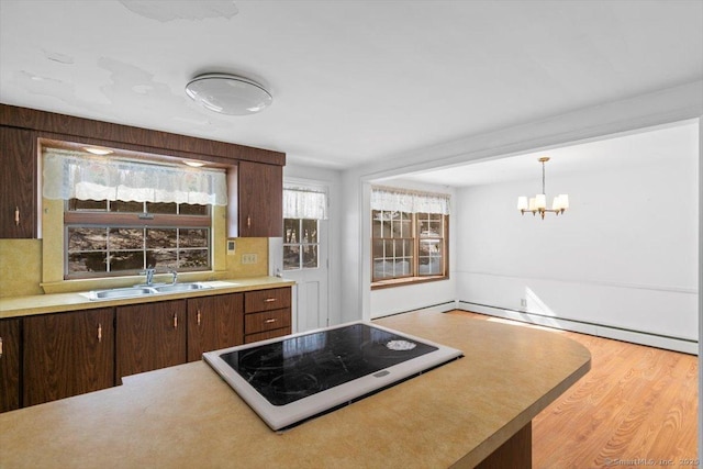 kitchen featuring light wood-style flooring, light countertops, baseboard heating, stovetop, and a sink