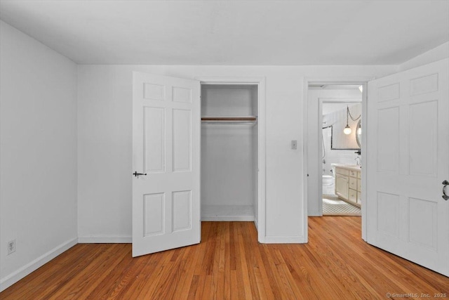 unfurnished bedroom featuring light wood-style flooring, baseboards, and a closet