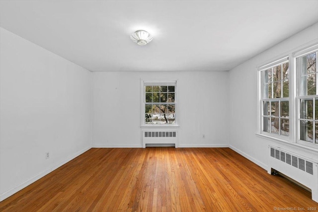 spare room with radiator heating unit, wood finished floors, and baseboards