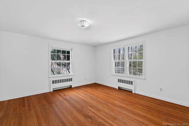 empty room with radiator heating unit, hardwood / wood-style flooring, and baseboards