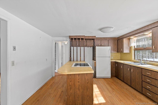 kitchen featuring light wood finished floors, freestanding refrigerator, black electric stovetop, light countertops, and a sink