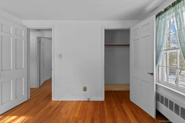 unfurnished bedroom with radiator, baseboards, a closet, and wood finished floors