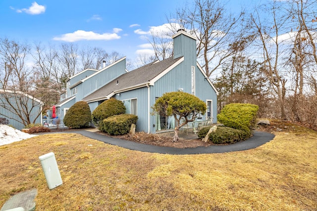 view of side of property with a chimney, a lawn, and roof with shingles