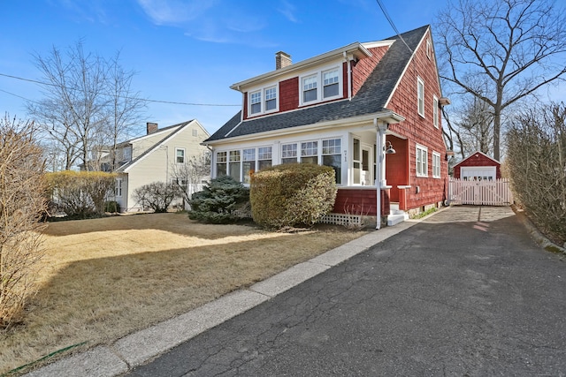 view of front of home with a gate, fence, driveway, roof with shingles, and a chimney