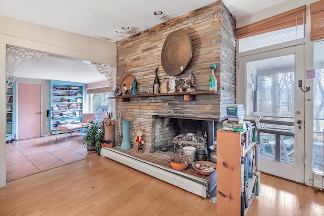 living area featuring a stone fireplace, baseboard heating, and wood finished floors