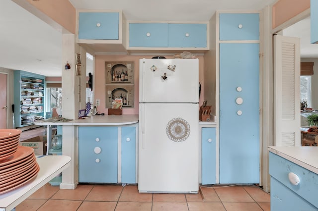 kitchen with light countertops, light tile patterned flooring, freestanding refrigerator, and blue cabinets