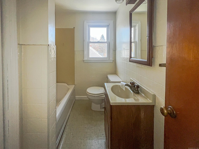 full bathroom with toilet, a wainscoted wall, a bathtub, vanity, and tile walls