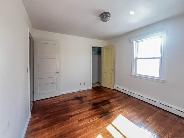 unfurnished bedroom with a baseboard heating unit, a closet, wood finished floors, and baseboards