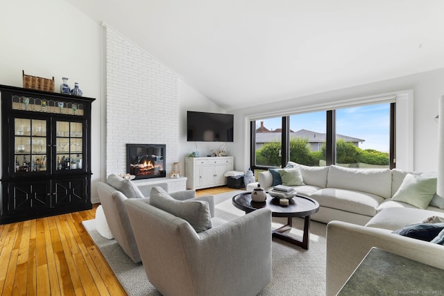 living area with high vaulted ceiling, a fireplace, and light wood-style flooring