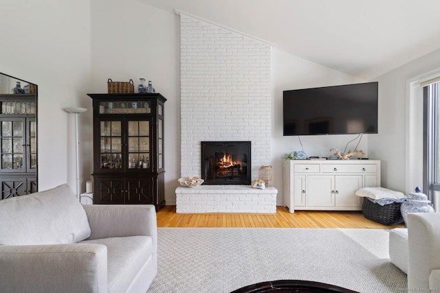 living room featuring lofted ceiling, light wood finished floors, and a brick fireplace