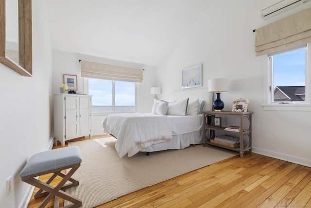 bedroom featuring baseboards, a wall unit AC, light wood-style flooring, baseboard heating, and vaulted ceiling