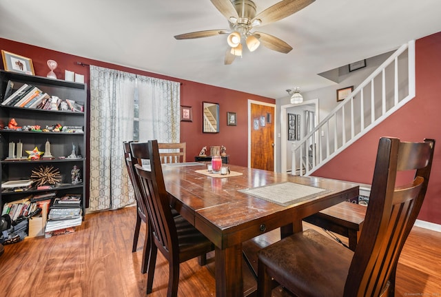 dining room with a ceiling fan, stairway, and wood finished floors