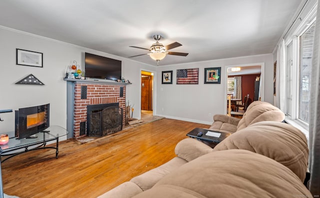 living room with crown molding, a fireplace, baseboards, and wood finished floors