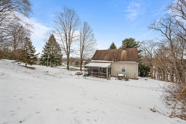 snow covered house featuring a sunroom and a chimney