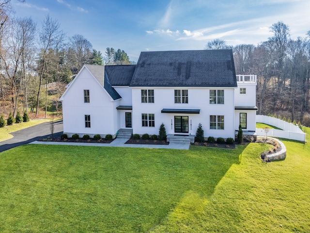 view of front of house featuring a shingled roof, fence, and a front lawn