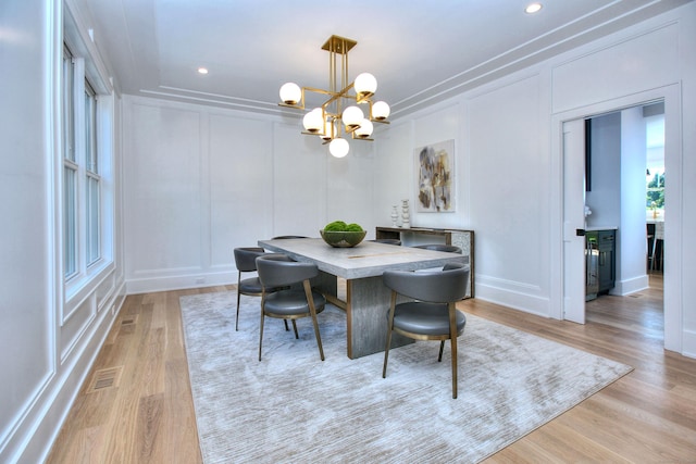 dining space with light wood finished floors, visible vents, a decorative wall, and a notable chandelier