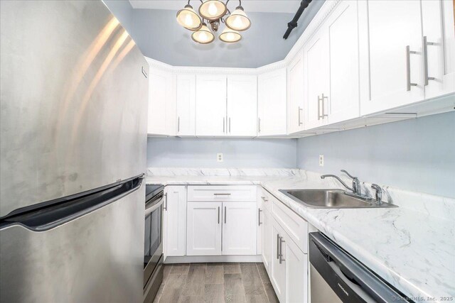 kitchen with stainless steel appliances, white cabinetry, a sink, and wood finished floors