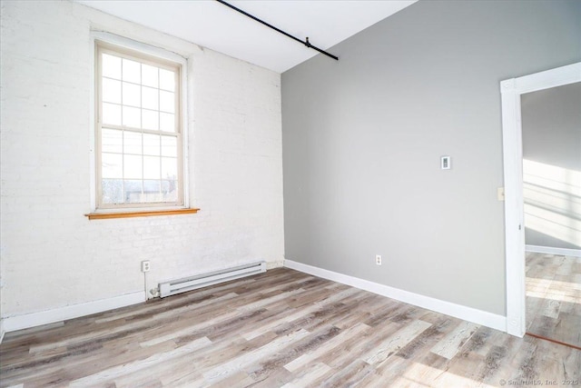 empty room featuring a baseboard heating unit, light wood-type flooring, brick wall, and baseboards