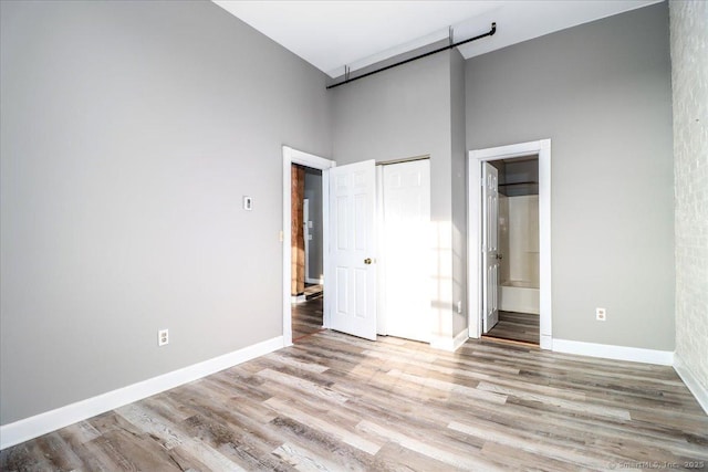 unfurnished bedroom with light wood finished floors, ensuite bath, a high ceiling, and baseboards