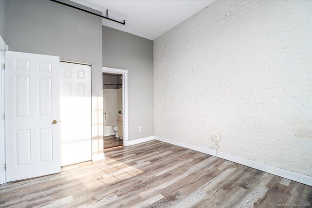 unfurnished bedroom with baseboards, ensuite bathroom, light wood finished floors, and a barn door