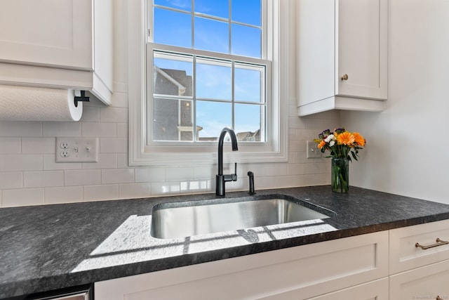 kitchen featuring dark stone counters, white cabinets, a sink, and decorative backsplash