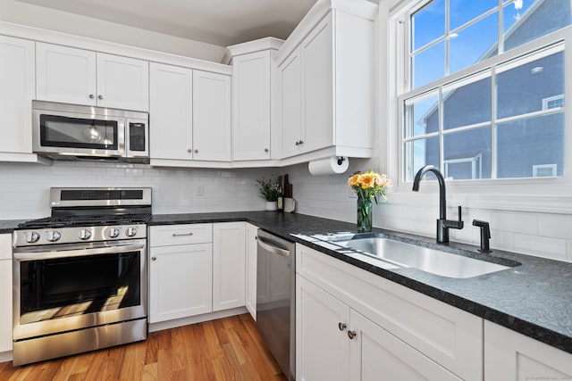 kitchen with appliances with stainless steel finishes, backsplash, a sink, and white cabinets