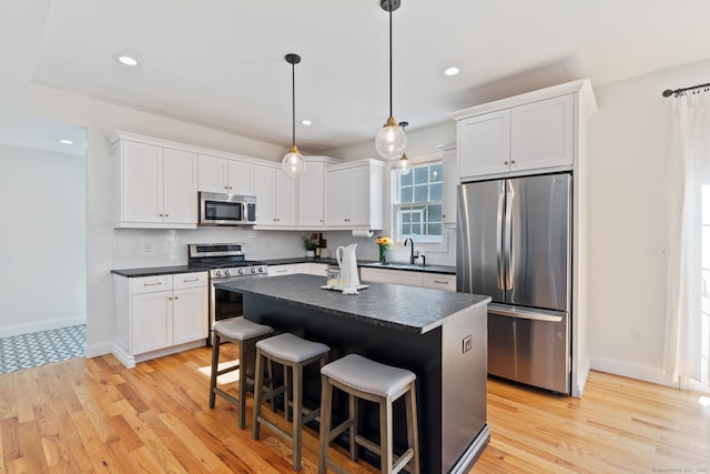 kitchen with decorative backsplash, white cabinets, dark countertops, appliances with stainless steel finishes, and a sink