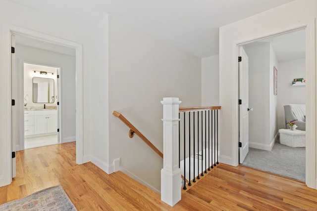 hall featuring baseboards, a sink, light wood-style flooring, and an upstairs landing