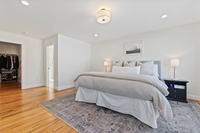 bedroom featuring light wood finished floors, baseboards, a walk in closet, a closet, and recessed lighting