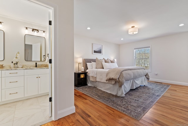 bedroom featuring light wood-type flooring, baseboards, a sink, and ensuite bathroom