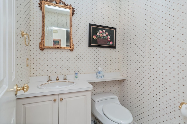 bathroom with vanity, toilet, and wallpapered walls