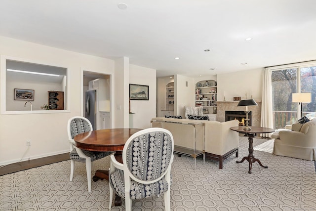dining room featuring baseboards, recessed lighting, a lit fireplace, and built in shelves