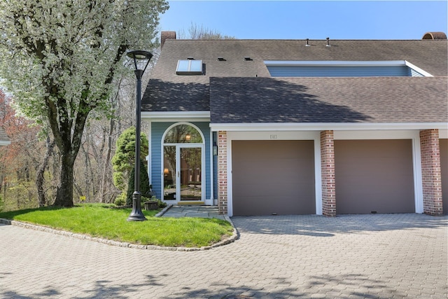 view of front facade featuring roof with shingles, a front lawn, brick siding, a garage, and decorative driveway
