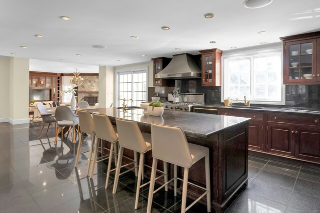 kitchen featuring stove, a kitchen island, wall chimney exhaust hood, dark countertops, and glass insert cabinets