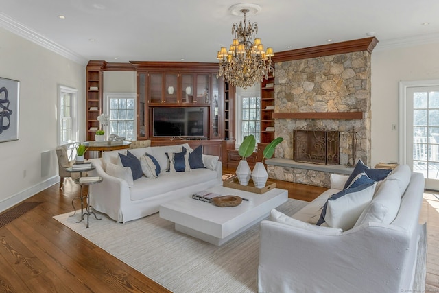 living room with crown molding, an inviting chandelier, a stone fireplace, wood finished floors, and baseboards