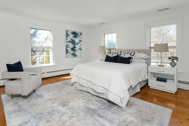 bedroom with crown molding, visible vents, baseboard heating, and wood finished floors