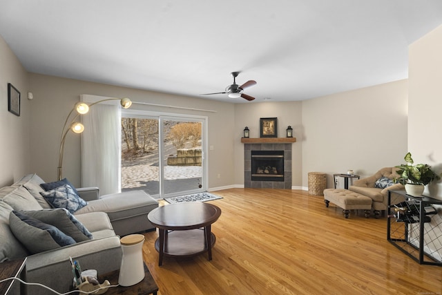 living area with a tiled fireplace, wood finished floors, a ceiling fan, and baseboards