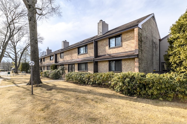 rear view of house with brick siding, a lawn, and a chimney