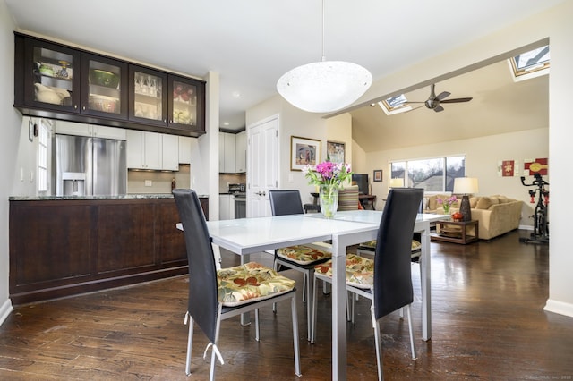 dining room featuring dark wood-type flooring, baseboards, lofted ceiling with skylight, and a ceiling fan