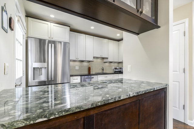 kitchen with white cabinets, appliances with stainless steel finishes, dark stone counters, and backsplash