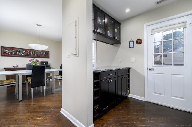 interior space featuring baseboards, light stone counters, glass insert cabinets, dark wood-type flooring, and dark cabinets