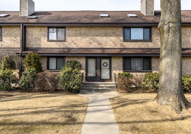 townhome / multi-family property with roof with shingles, brick siding, and a chimney