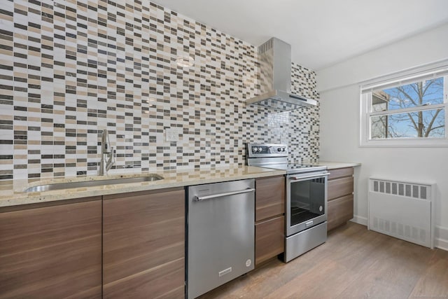 kitchen with stainless steel appliances, tasteful backsplash, radiator heating unit, a sink, and wall chimney range hood